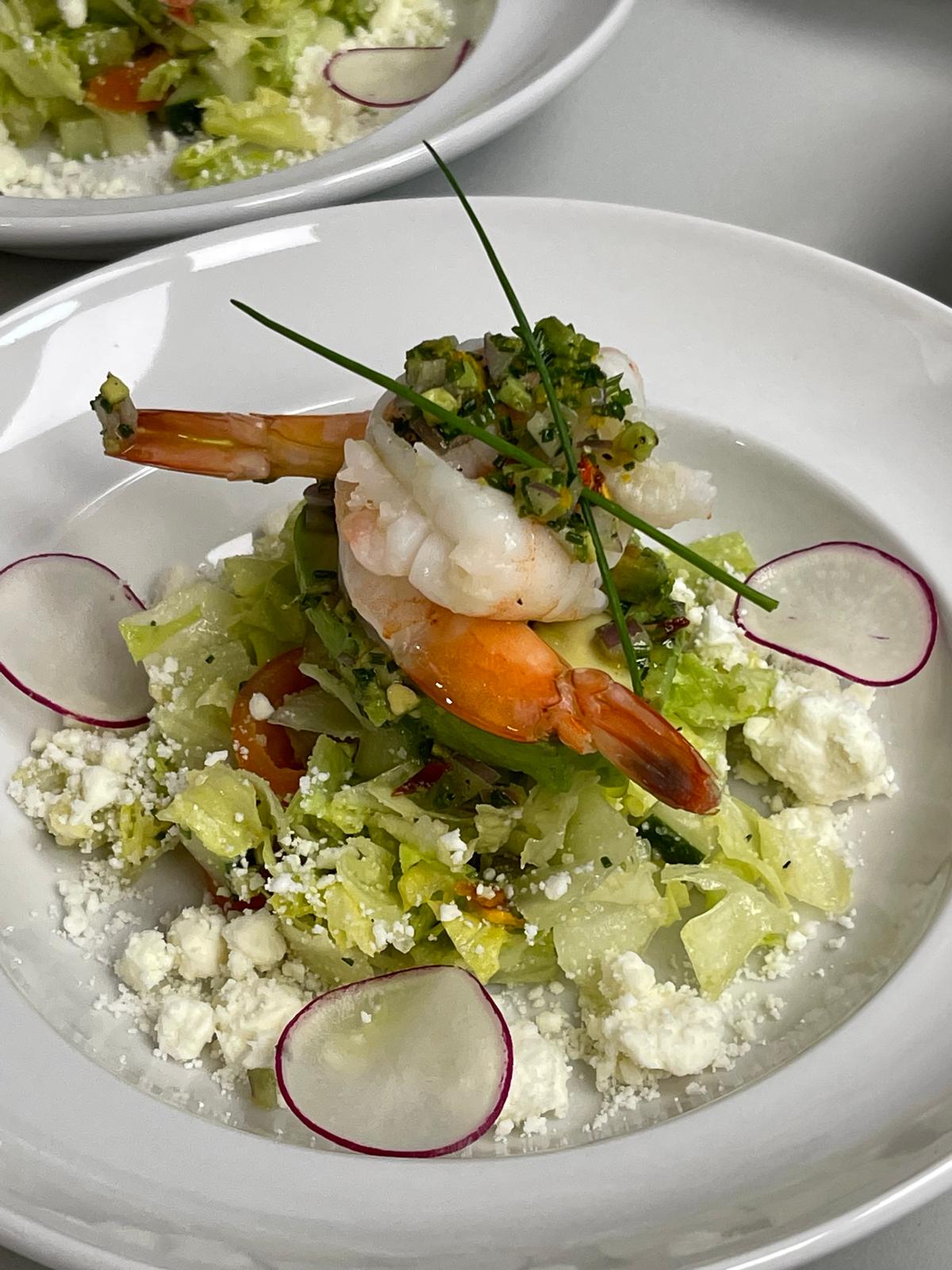 Shrimp salad with lettuce, radish slices, crumbled cheese, and herbs on a white plate.