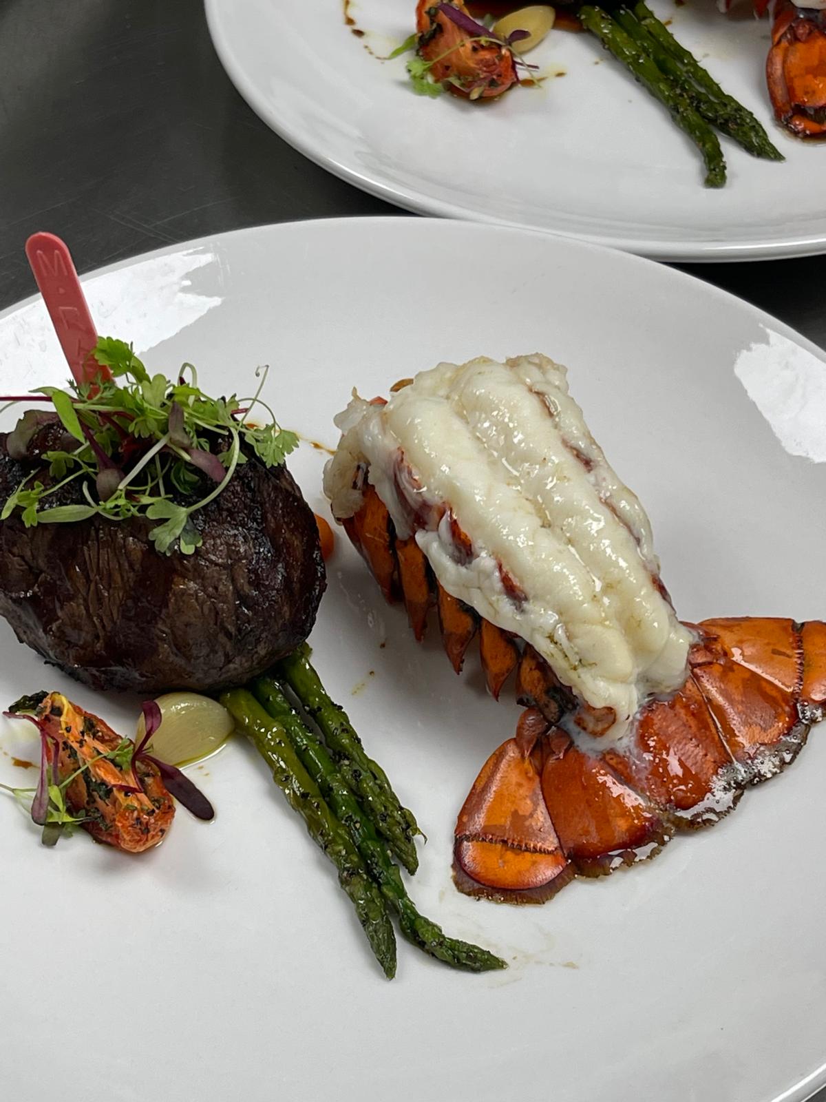 Plate with grilled steak, lobster tail, asparagus, and garnishes on a white dish.