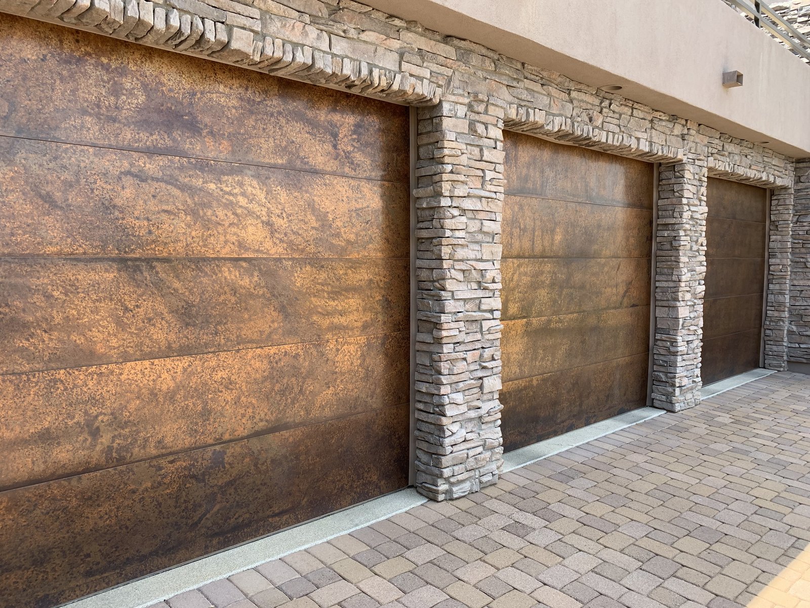 Three bay woodgrain garage doors between stone columns