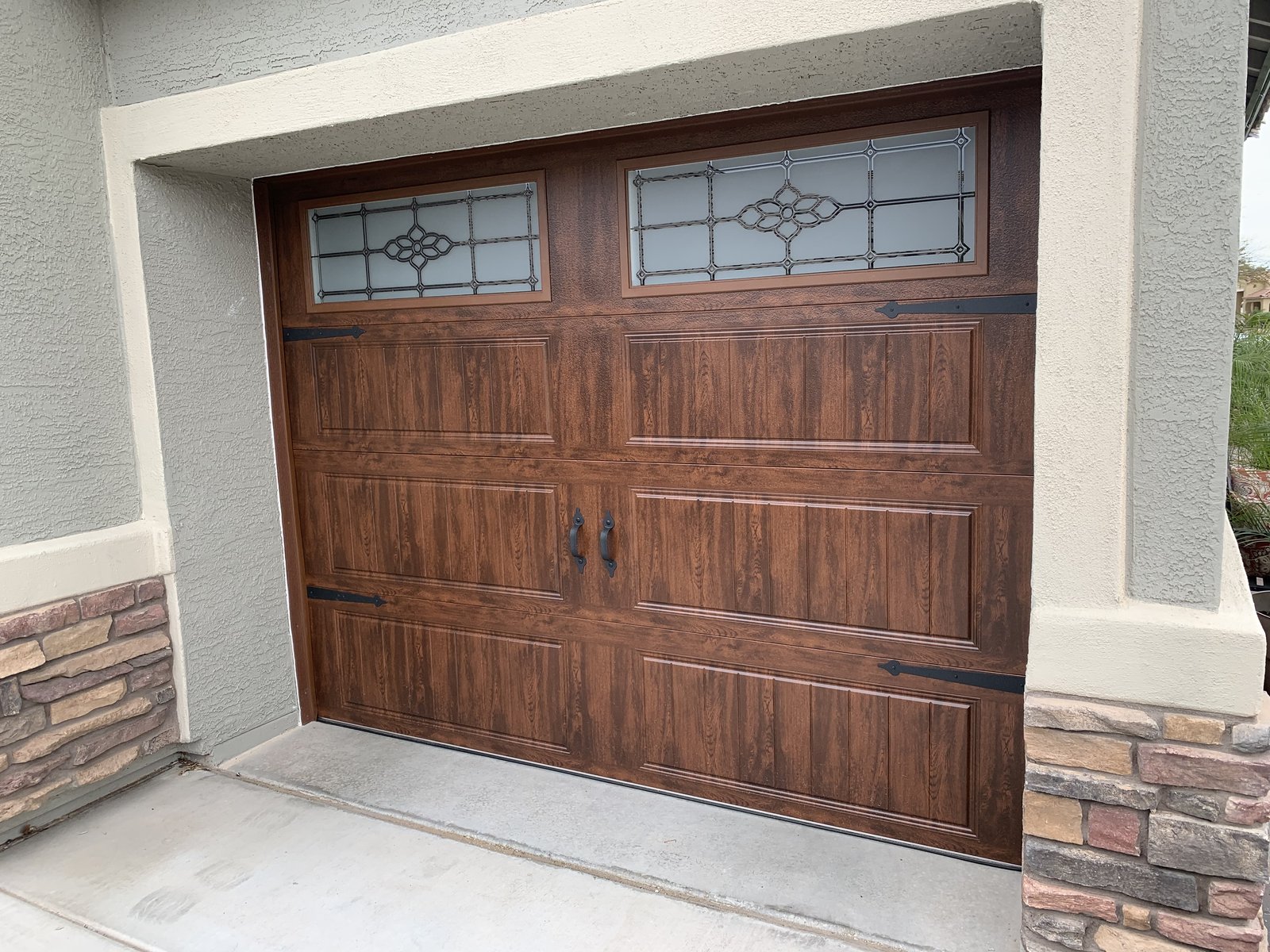 Woodgrain garage door with decorative windows and a stone accent wall