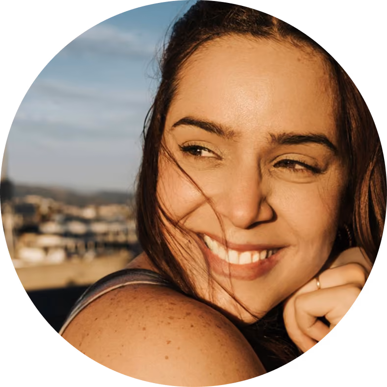 Smiling woman with brown hair looking to the side outdoors with blurred background.