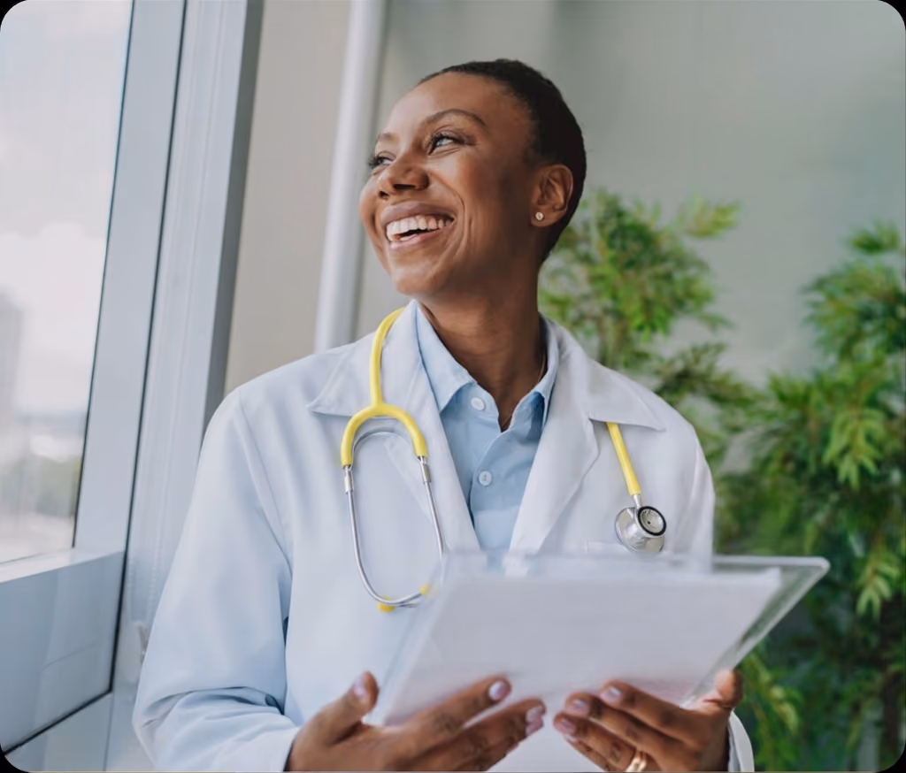 Smiling doctor with yellow stethoscope holding a clipboard near a window and plants.