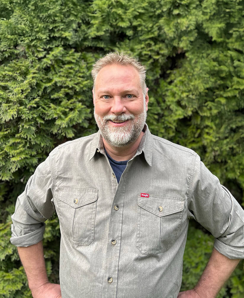 A photo of Mike Sherman standing by a cedar tree.