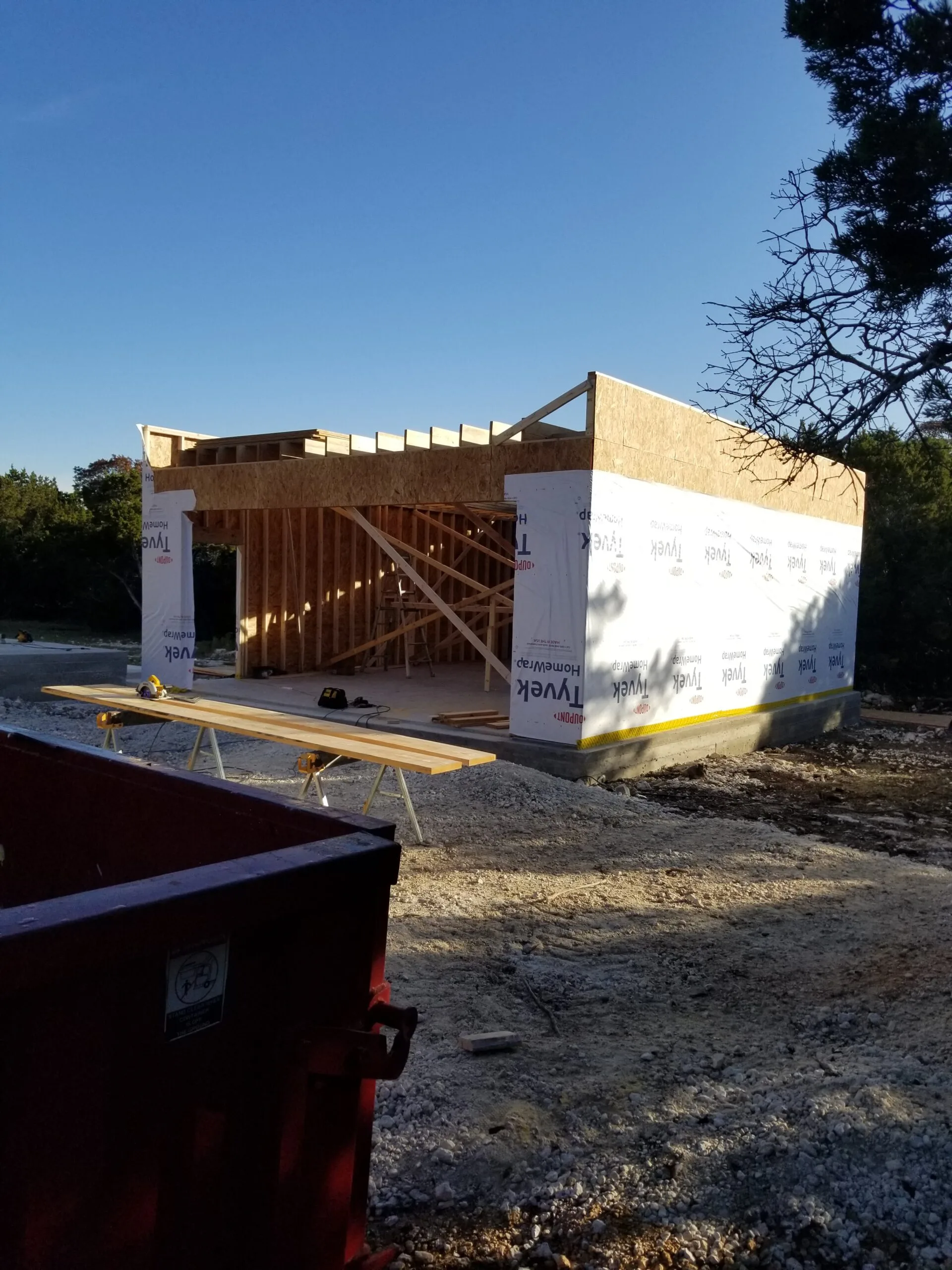 Housewrapped detached garage under construction with a dumpster on site