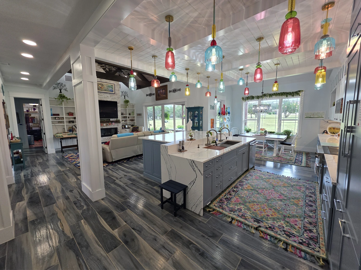 Open kitchen and living area with a stone fireplace, wood beams, and colored glass pendant lights