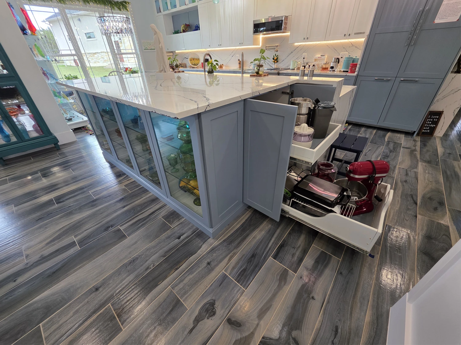 Quartzite waterfall island with glass display cabinetry and pull-out storage in the custom kitchen
