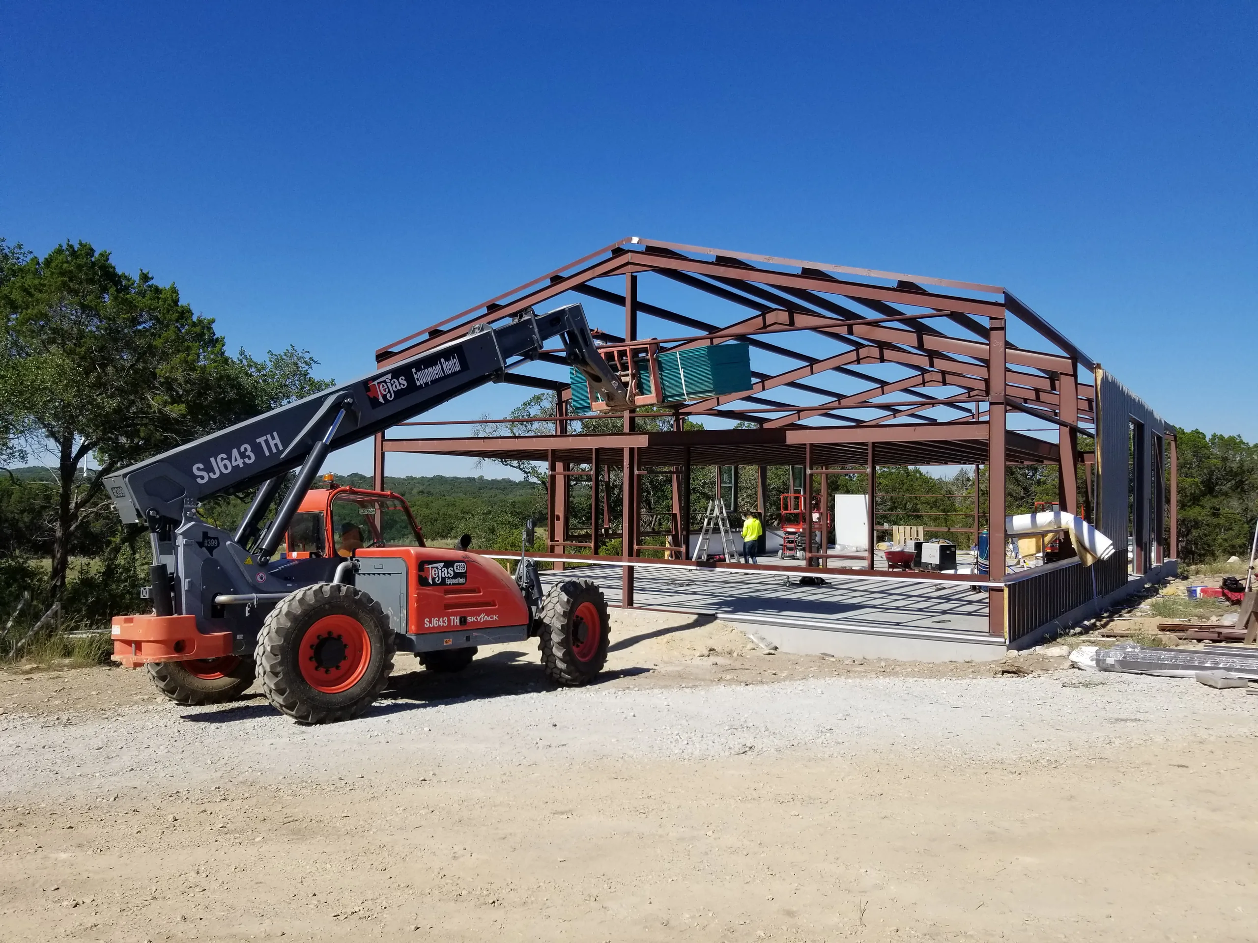 Telehandler parked alongside the steel frame while the crew sets wall panels