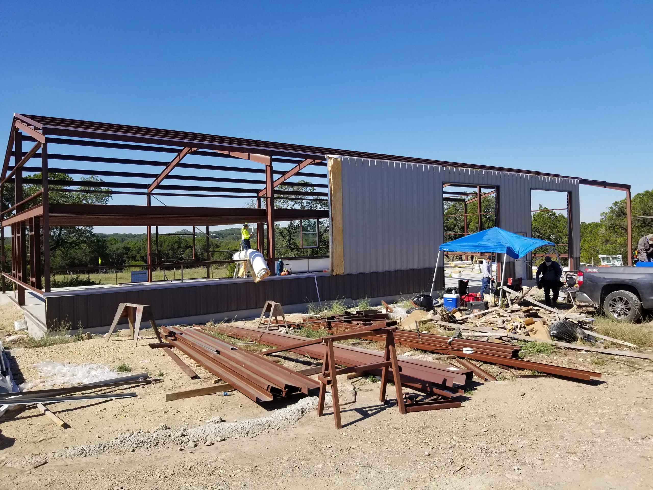 Steel purlins stacked on sawhorses in front of the frame as the first wall panels and door openings go in