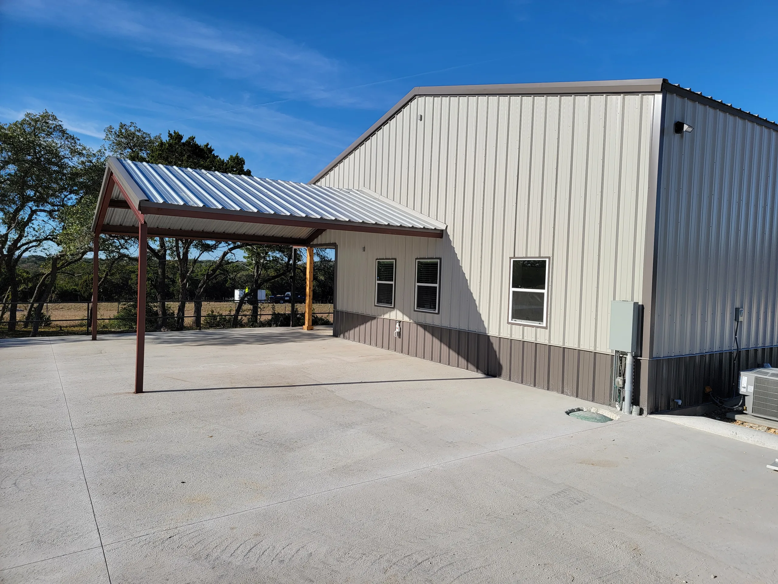 Gable end of the finished building with a covered pavilion and windows over a new concrete apron