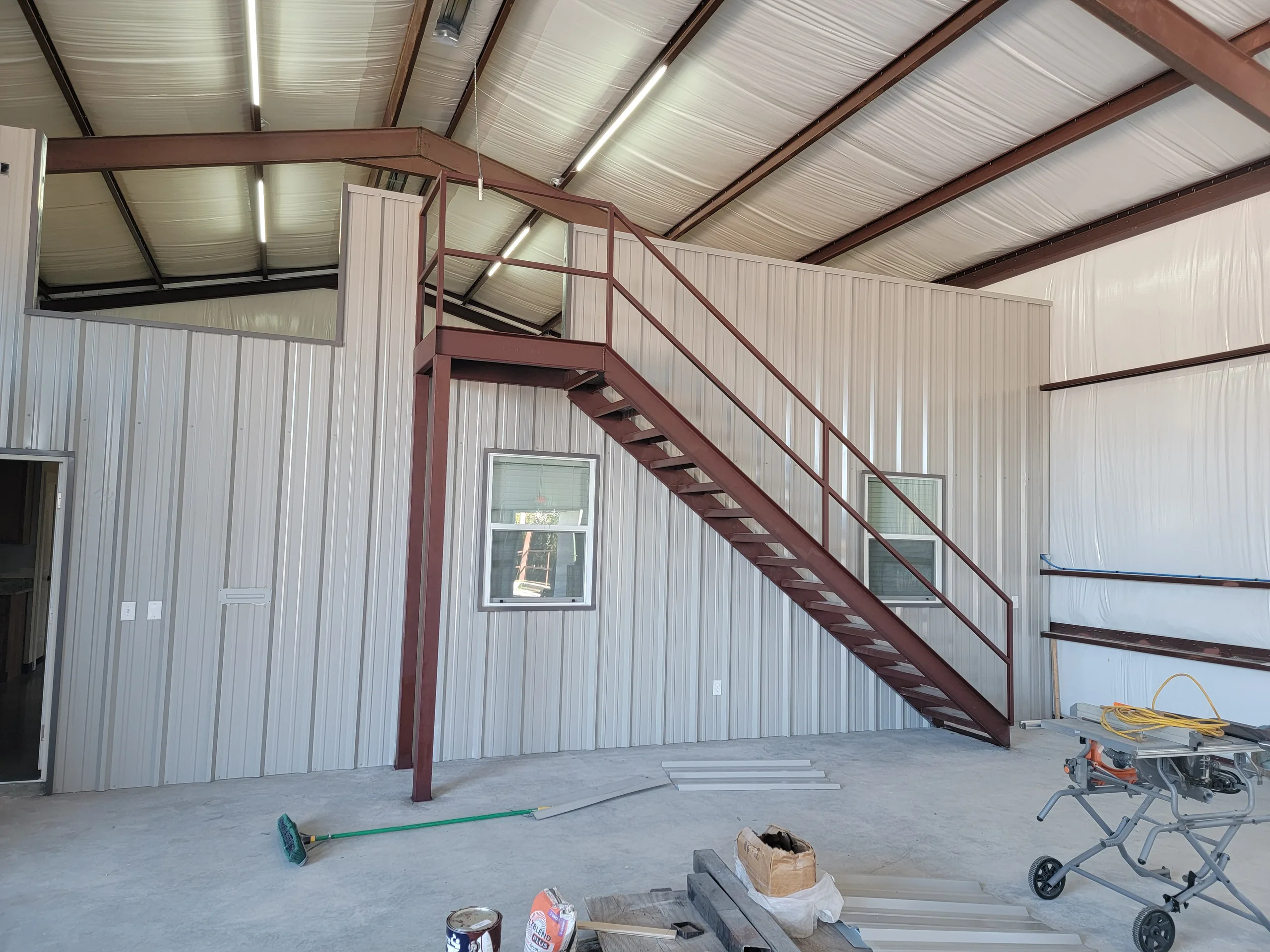 Finished steel building interior with a steel staircase up to a mezzanine and insulated white metal walls