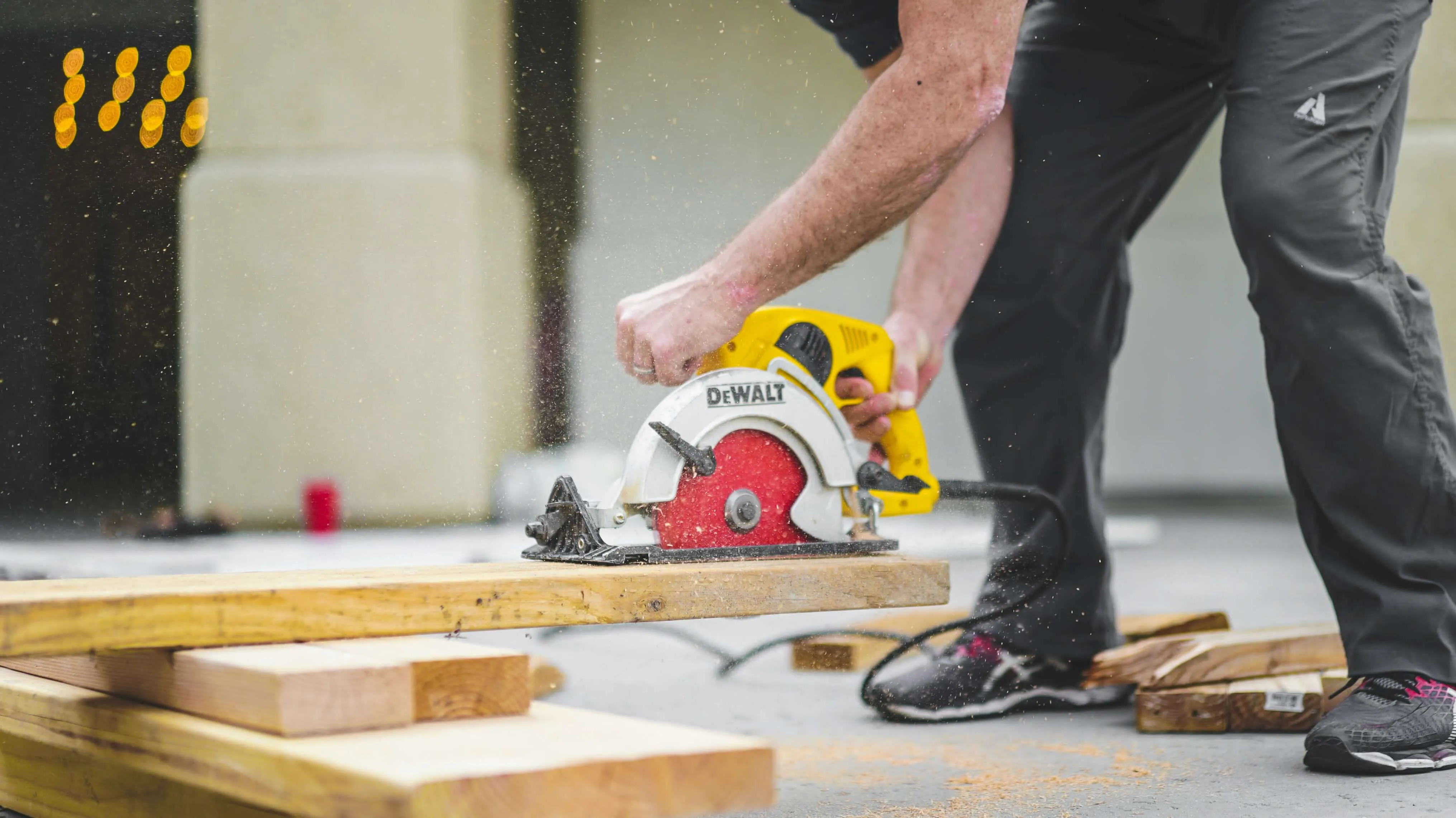 Person using yellow DeWalt circular saw to cut wooden boards on a concrete surface.