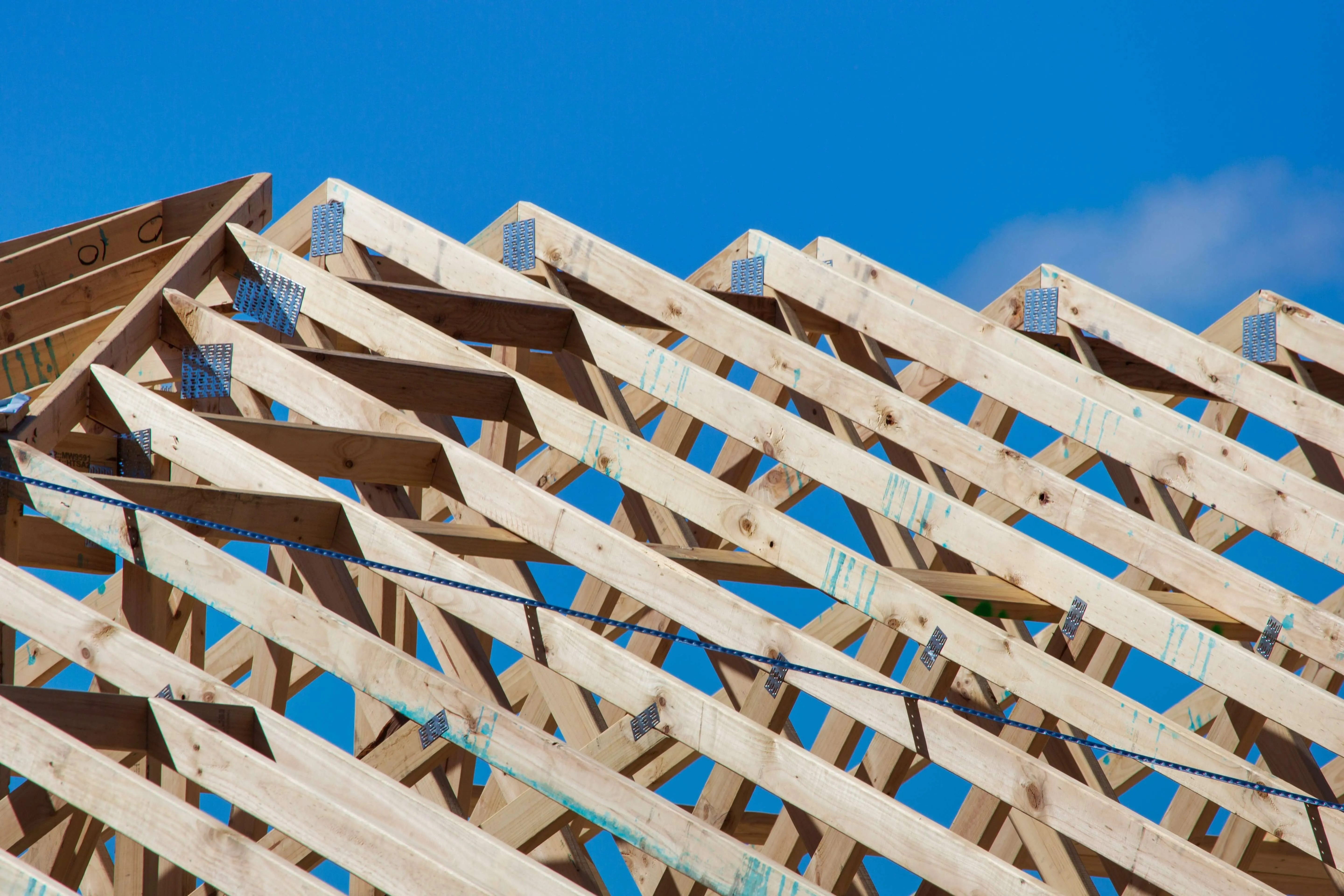 Wooden roof trusses under construction set against a clear blue sky.