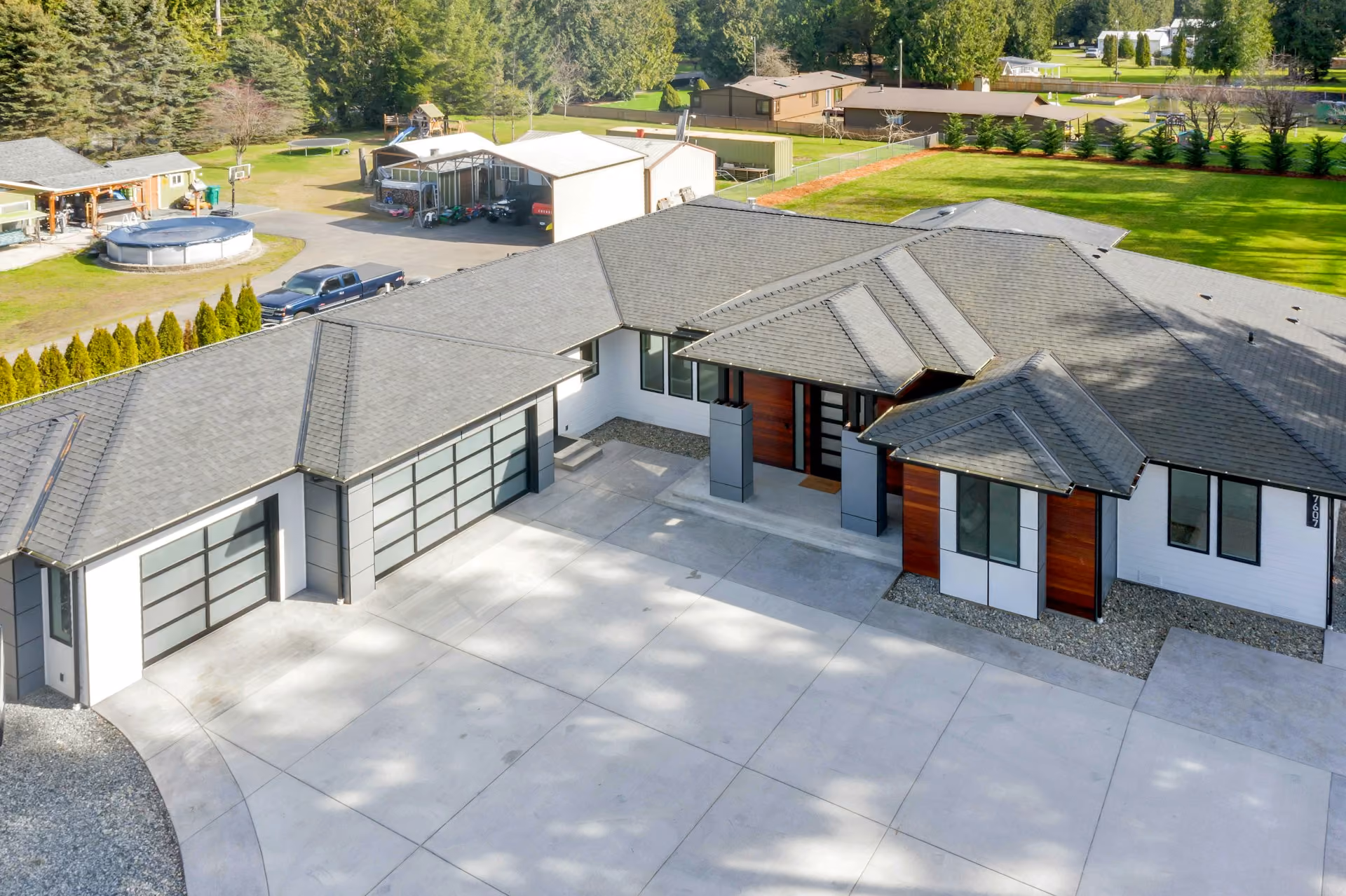 Modern single-story house with large concrete driveway and three-car garage surrounded by greenery.
