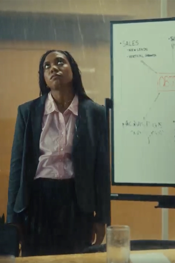 Woman in business attire standing indoors next to a whiteboard with sales notes, looking upward with a frustrated expression.