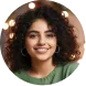 Smiling woman with curly hair wearing a green top against a blurred background with lights.