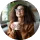 Smiling woman with curly hair holding a transparent glass mug with tea, sitting in a cozy setting.