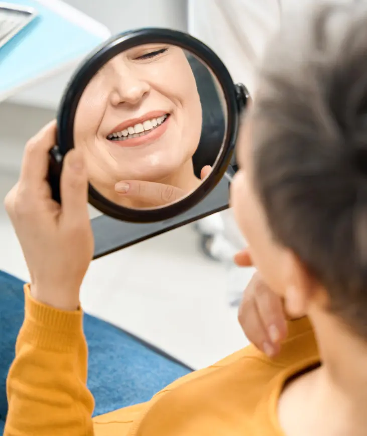 Person in mustard shirt smiling at their reflection while holding a round mirror.