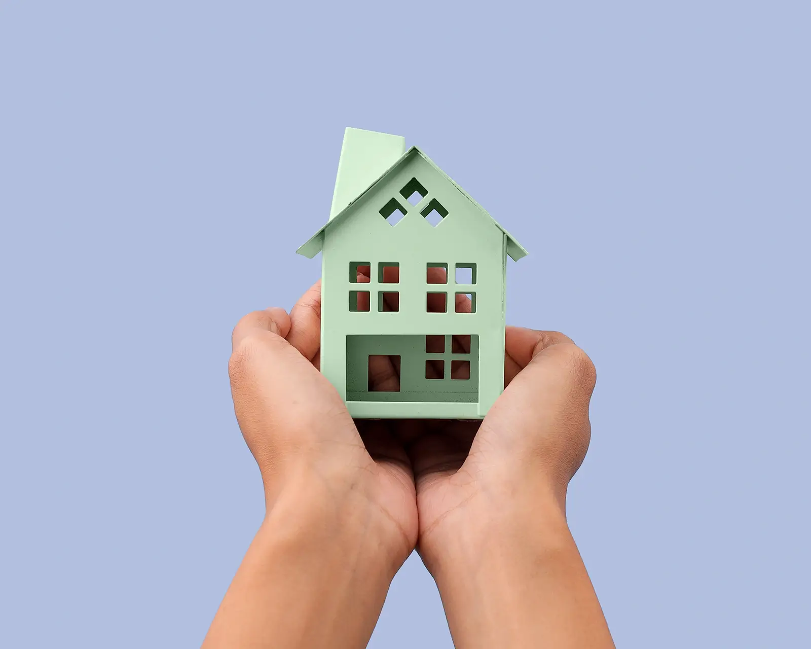 Cupped hands holding a green model house against a periwinkle background, symbolising home loan repayment planning