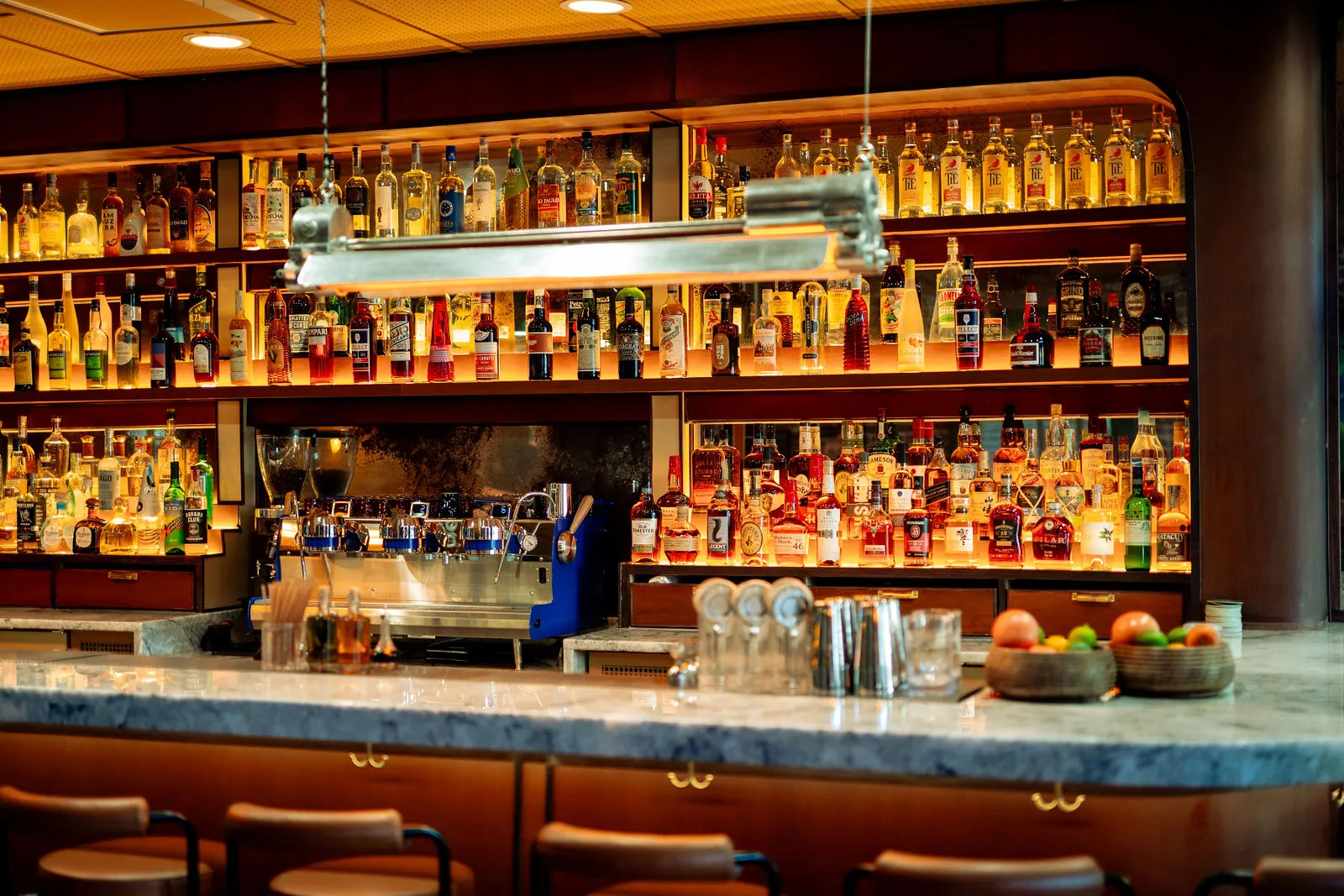 CANA's illuminated back bar with bottles, espresso machine, and marble counter