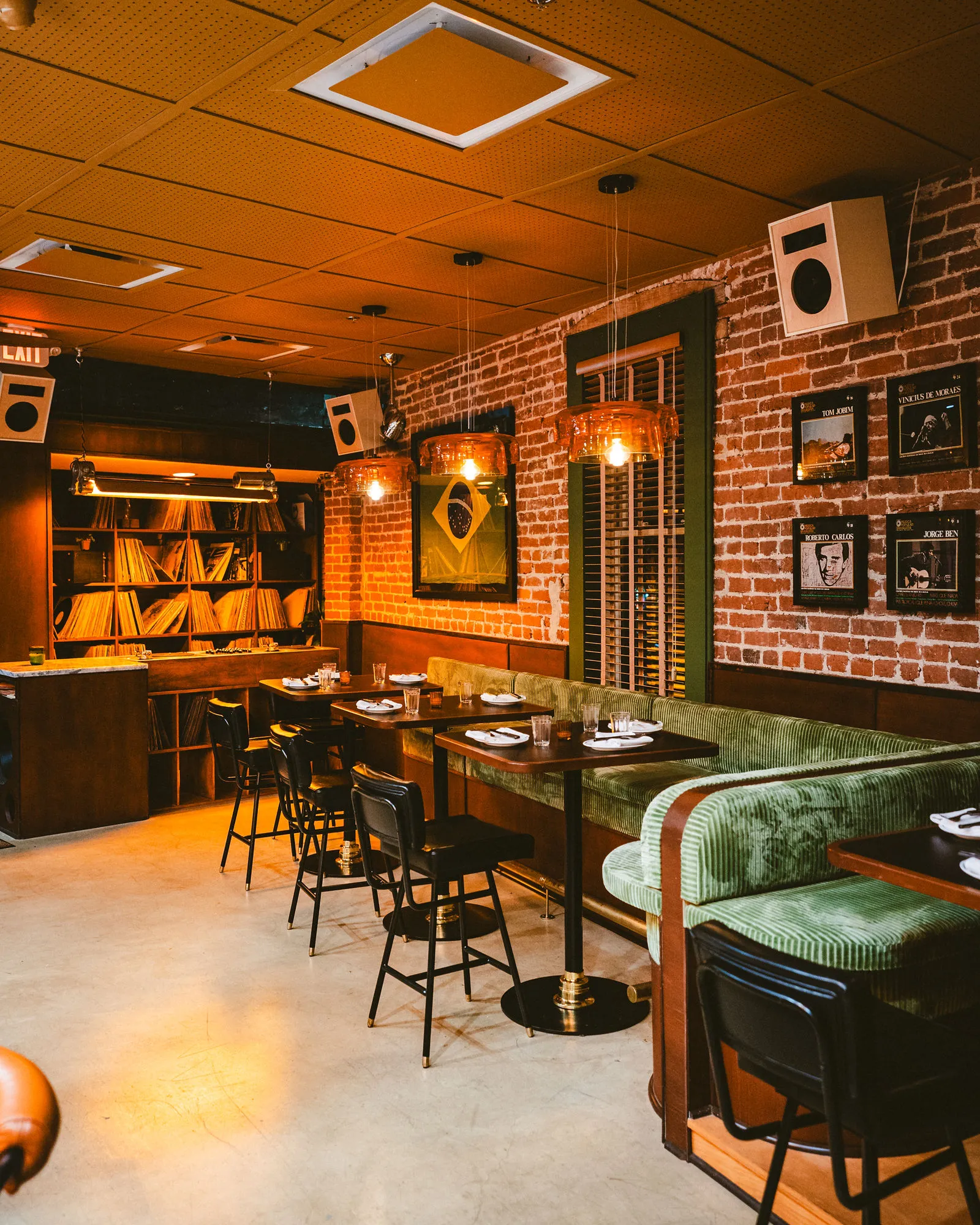 A full view across CANA's green banquettes, brick walls, record shelves, and amber-lit dining room