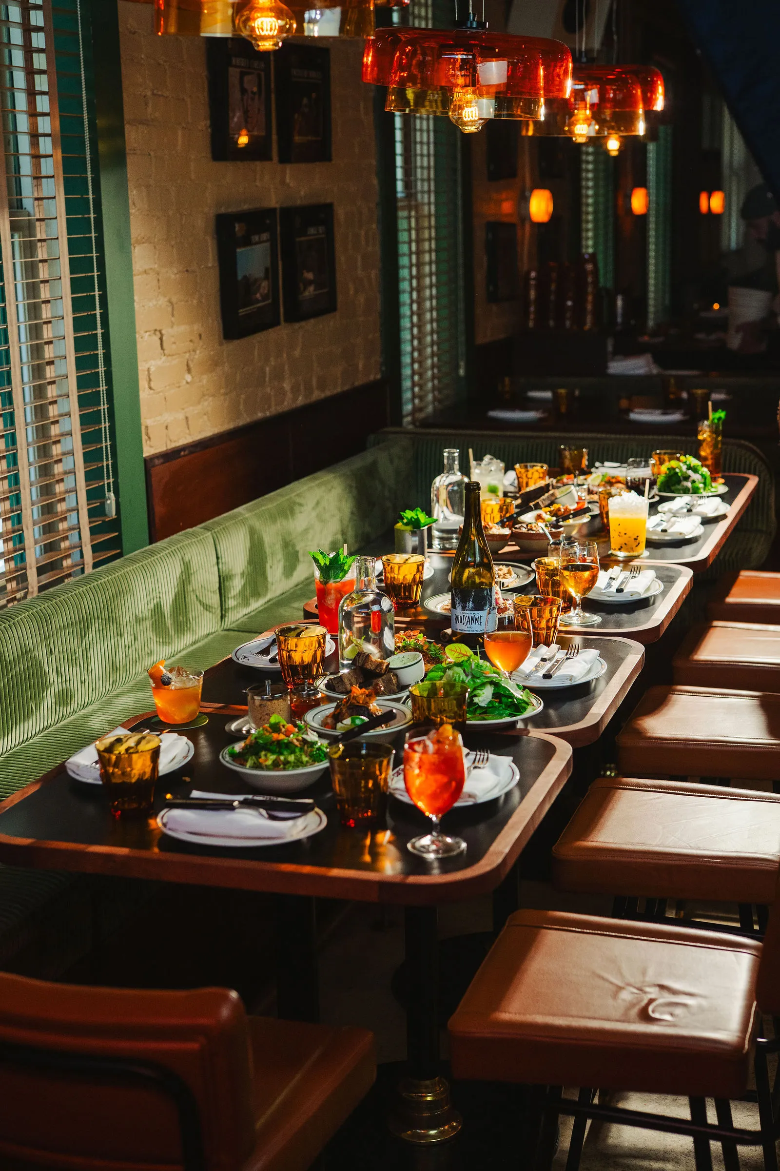 A long table at CANA set with shared plates, cocktails, and wine beneath amber lights