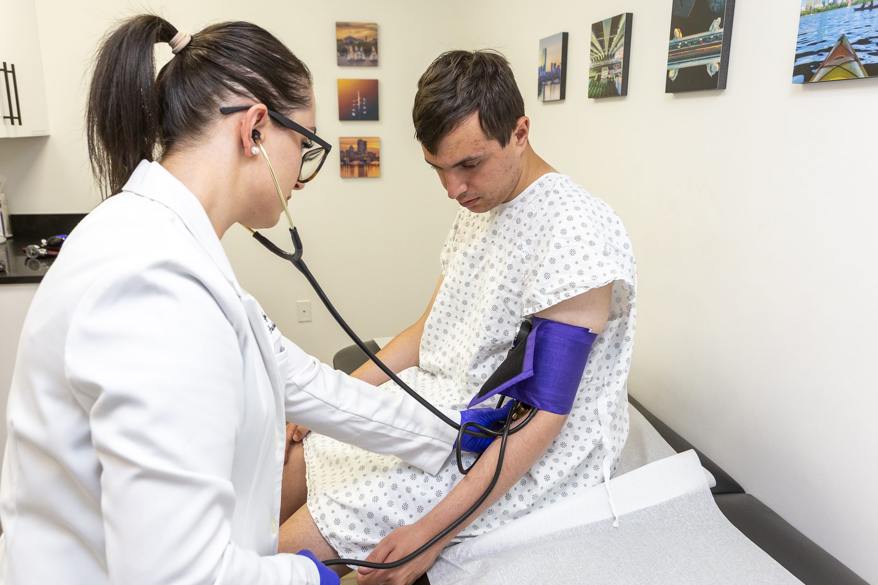 Healthcare professional measures blood pressure of young male patient in exam room.