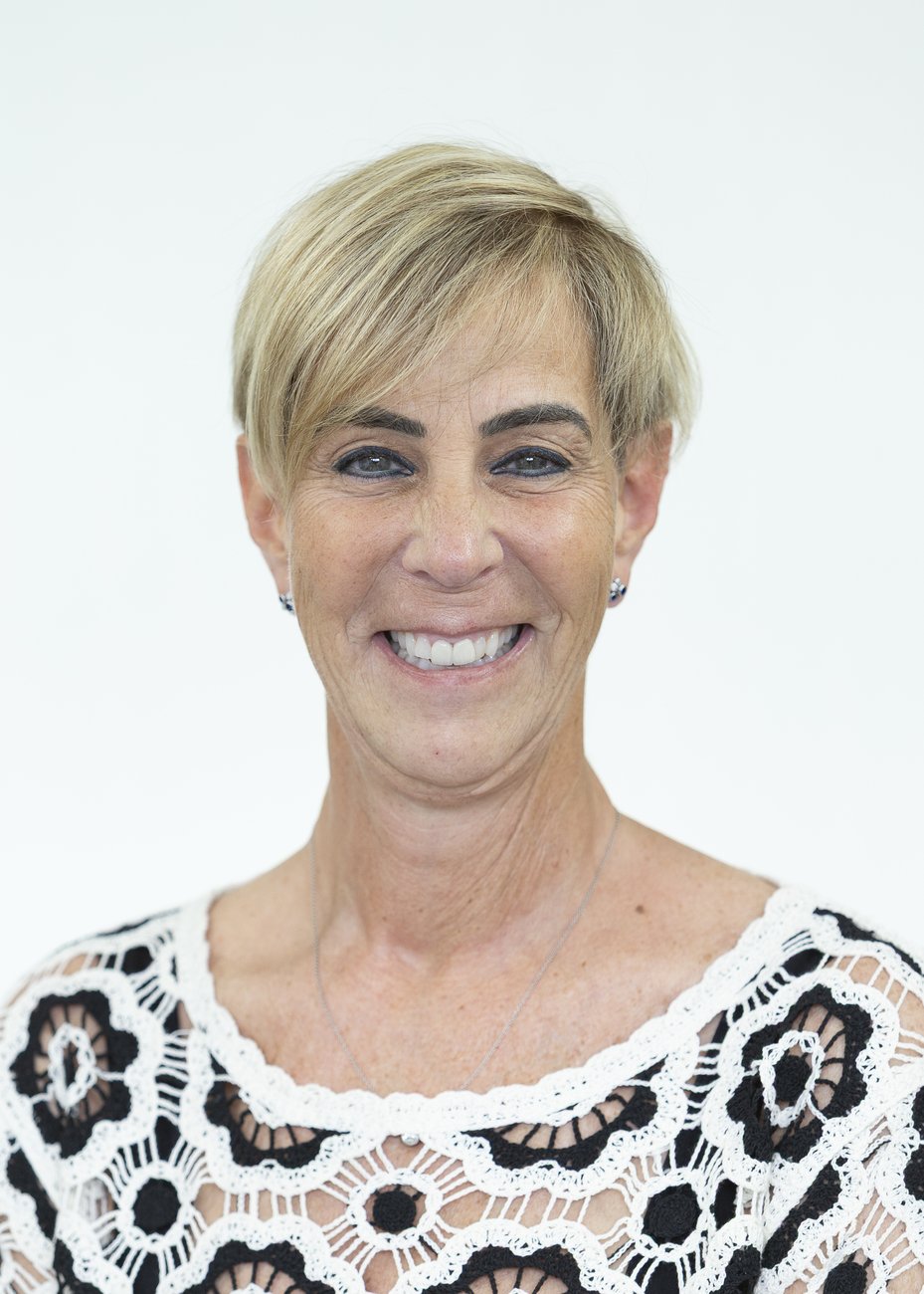 Smiling woman with short blonde hair wearing a black and white lace top against a plain background.