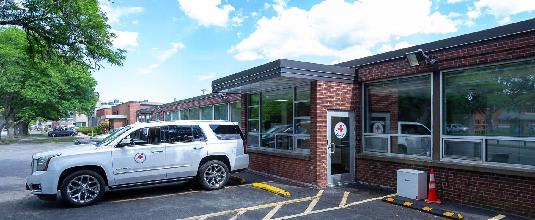 White SUV with red cross parked outside a red brick clinic building on a sunny day.