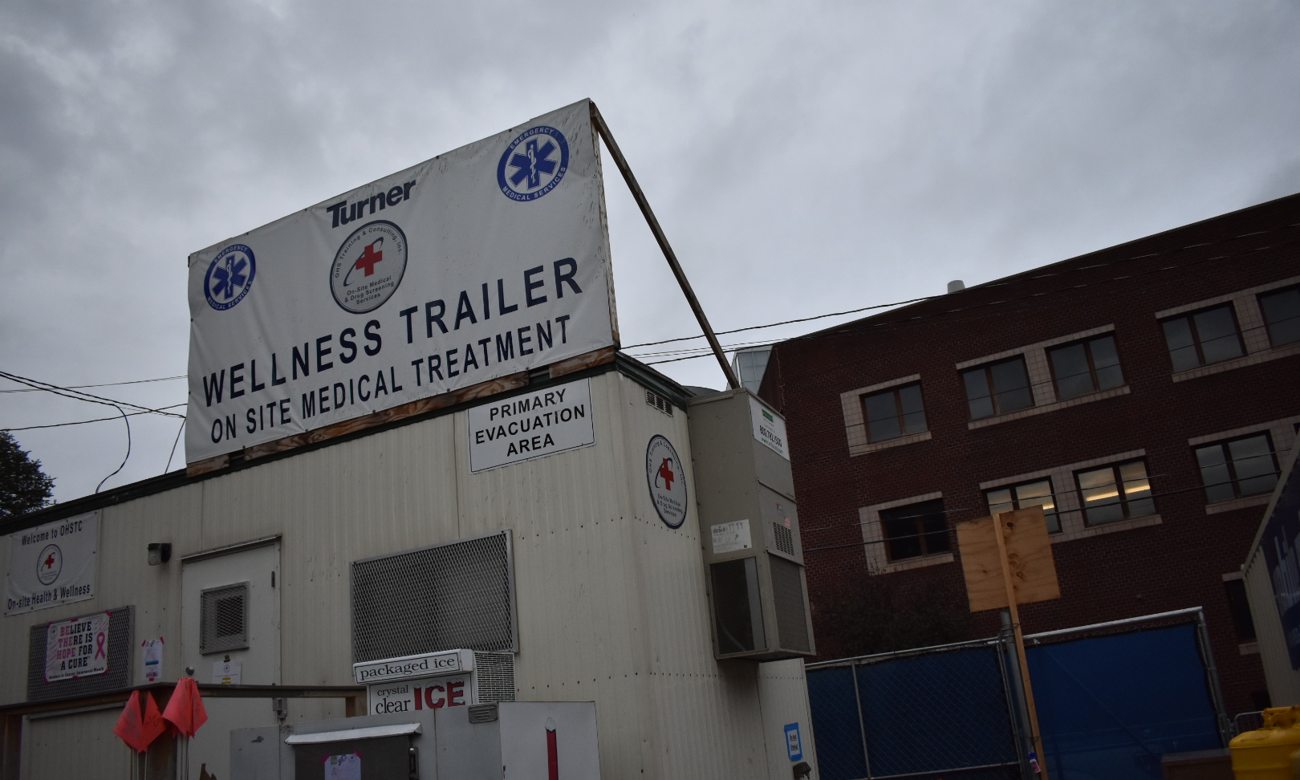 White wellness trailer with signs for on-site medical treatment and primary evacuation area under gray cloudy sky.