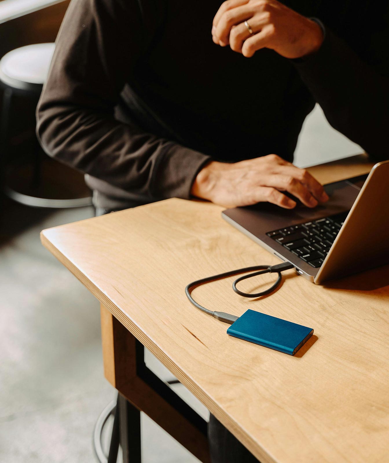 Person typing on a laptop connected to a blue Samsung external SSD on a wooden table with a glass of coffee nearby.
