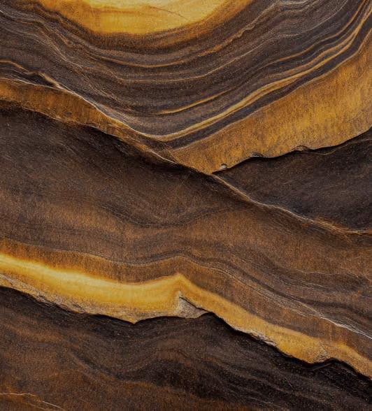 Close-up of a textured rock surface with layered brown, yellow, and dark brown strata creating a natural, wavy pattern.