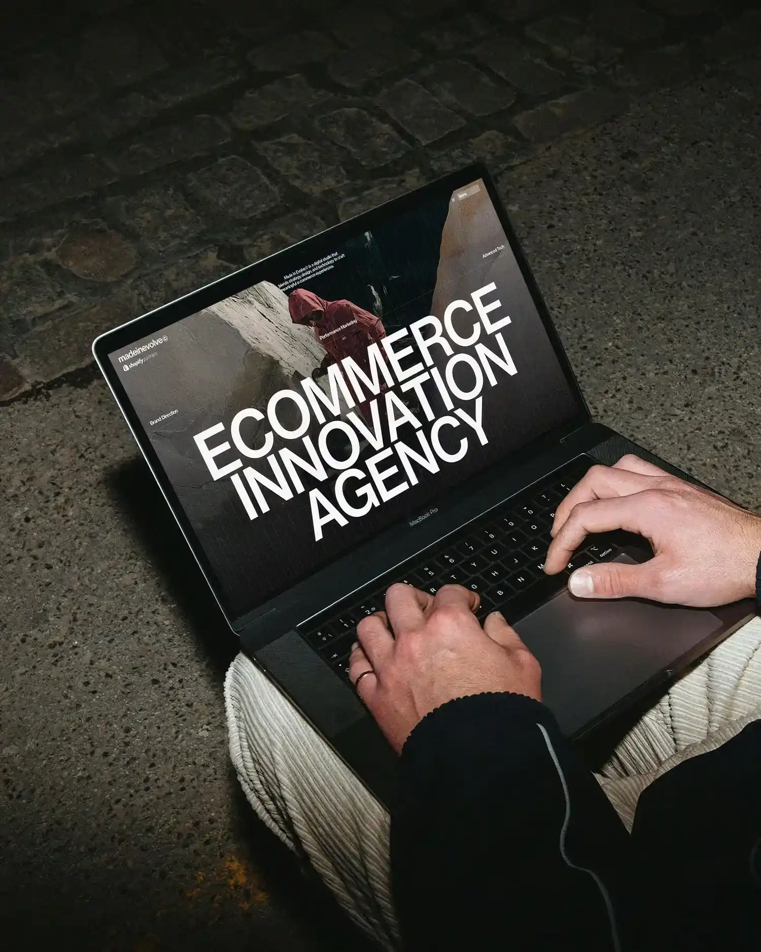 Hands typing on a MacBook Pro showing a screen with 'Ecommerce Innovation Agency' text.