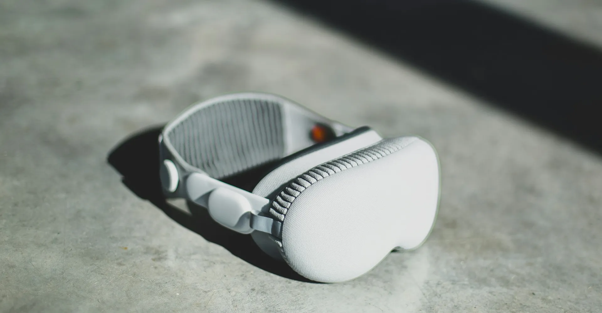 White and gray VR headset placed on a concrete floor with soft lighting and shadows.