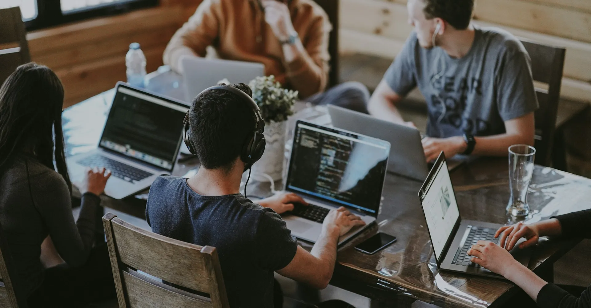 Four people working on laptops at a wooden table in a casual office setting.