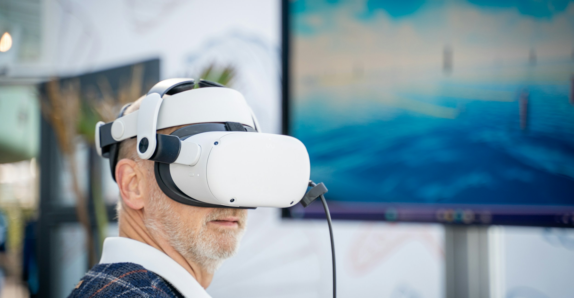 Older man wearing a white VR headset with a blurred screen showing water in the background.