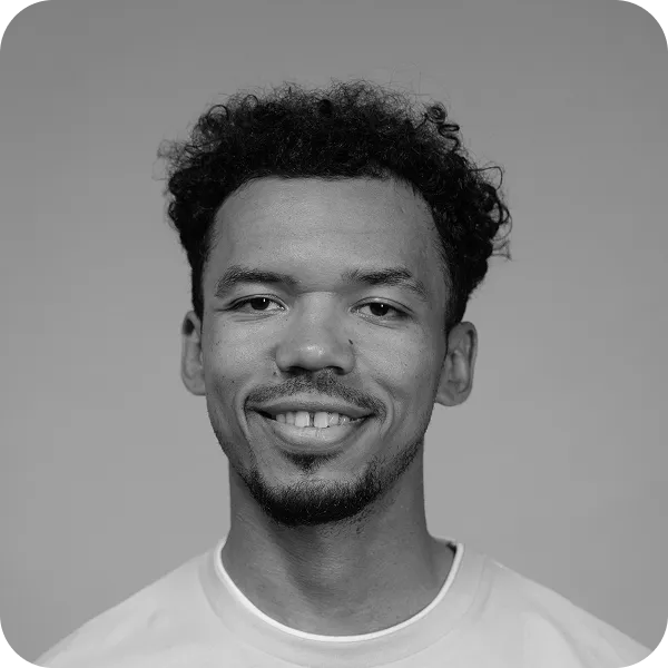 Young man with curly hair and goatee smiling at the camera, wearing a light-colored shirt.