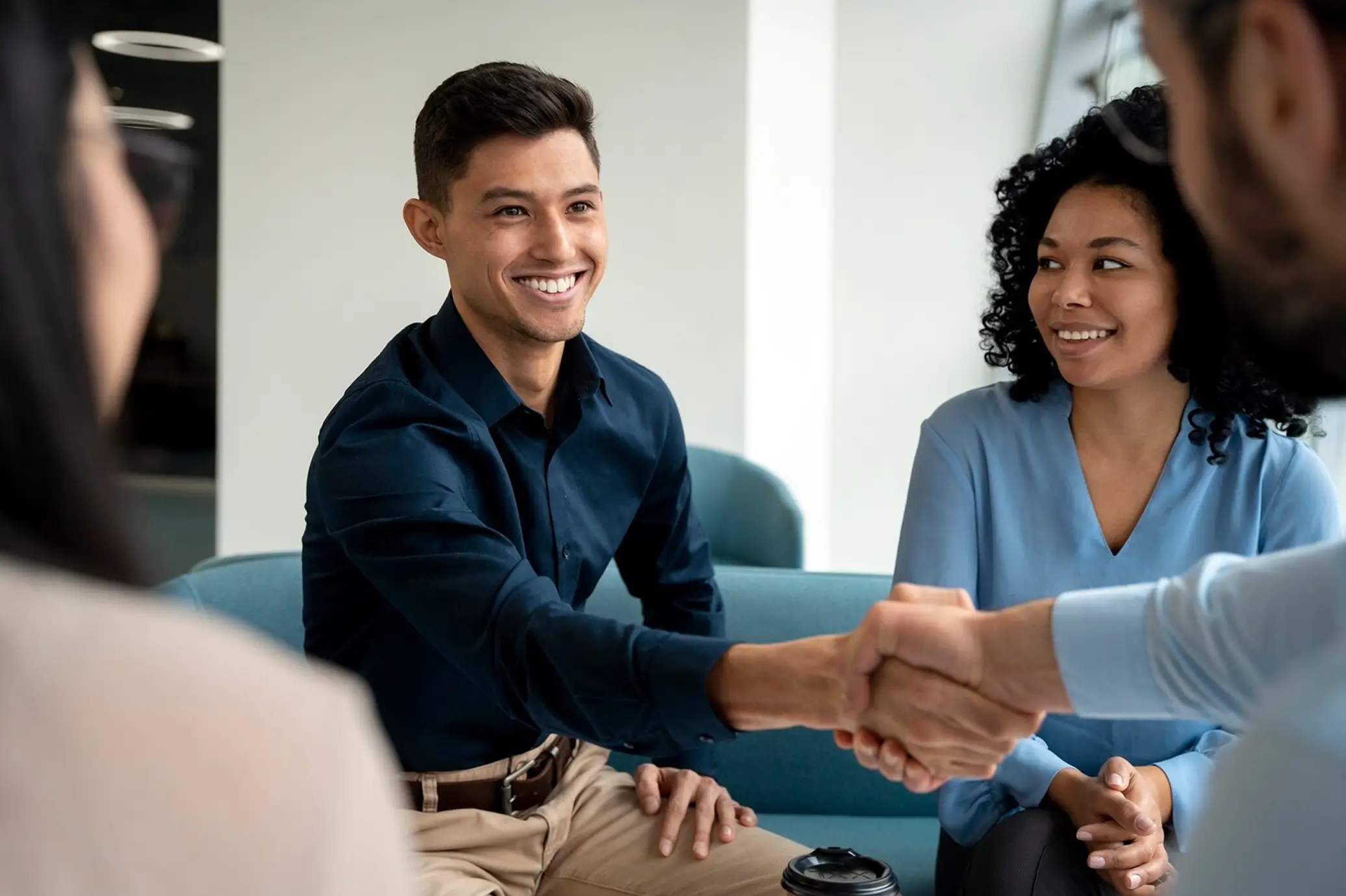 Smiling young man shaking hands with another person while a woman nearby watches and smiles.