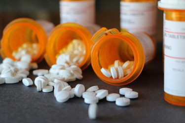 White tablets spill from open orange prescription bottles onto a dark surface.