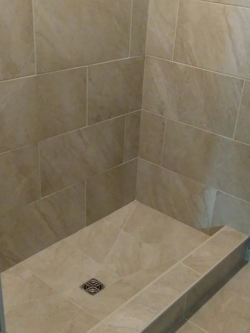 Travertine walk-in shower with a low curb and a centre drain, installed by Euphoric Tile & Design in coastal Maine