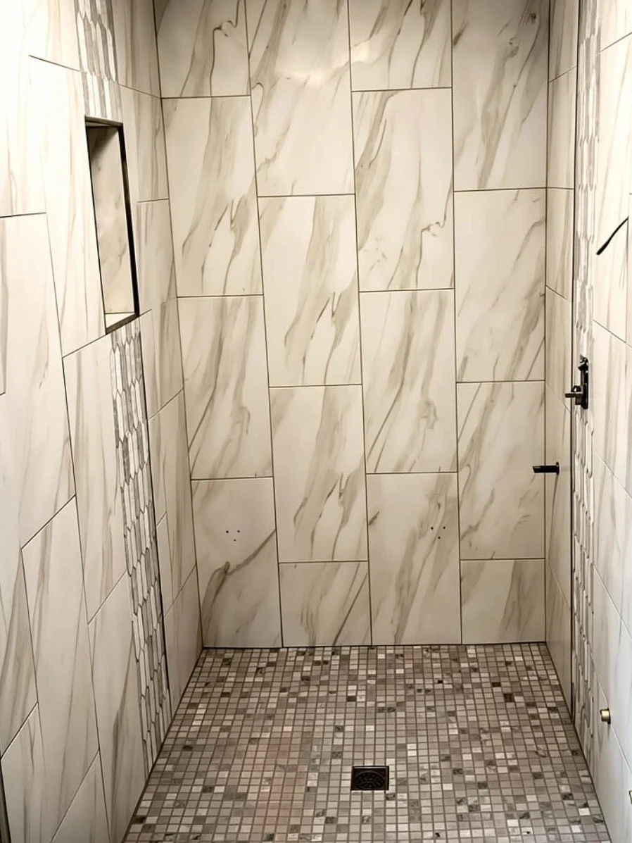 Walk-in shower finished in marble-look porcelain, with a mosaic tile floor and a recessed wall niche, installed by Euphoric Tile & Design in coastal Maine