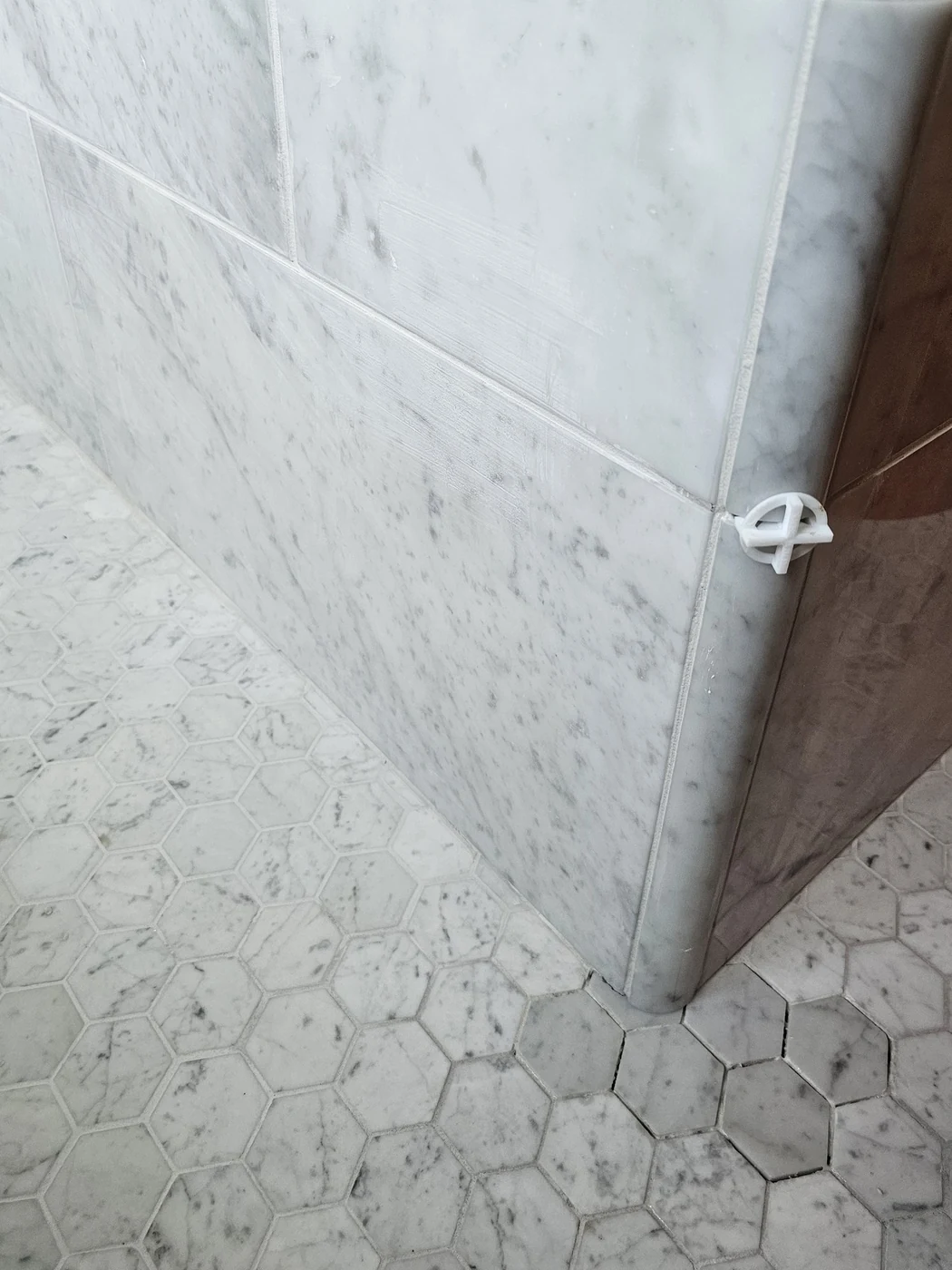 Carrara marble wall meeting a hexagonal tile floor, joints held true through the corner, installed by Euphoric Tile & Design in coastal Maine
