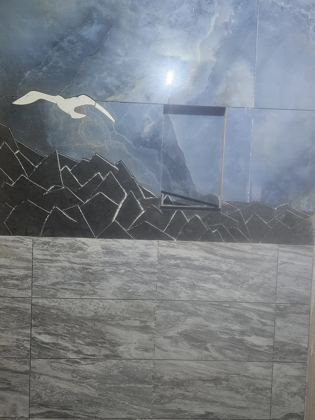 Custom tile mural of an ocean scene, cut and set by hand, framed by a stone-look surround, installed by Euphoric Tile & Design in coastal Maine