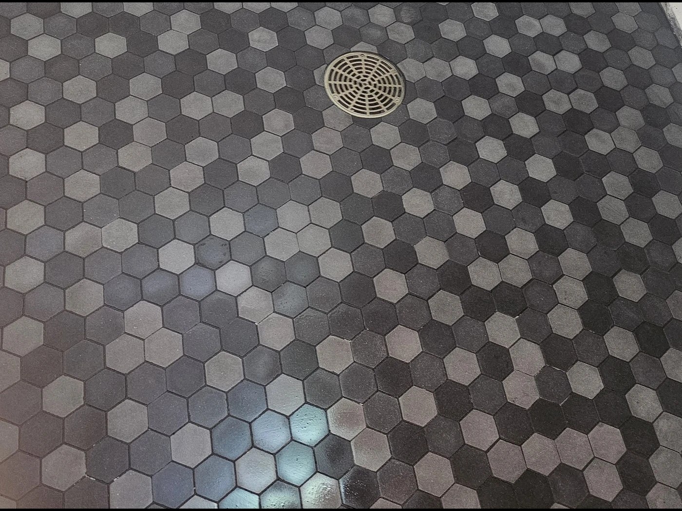 Floor with hexagonal gray tiles arranged in a pattern and a round metal drain cover near the center.