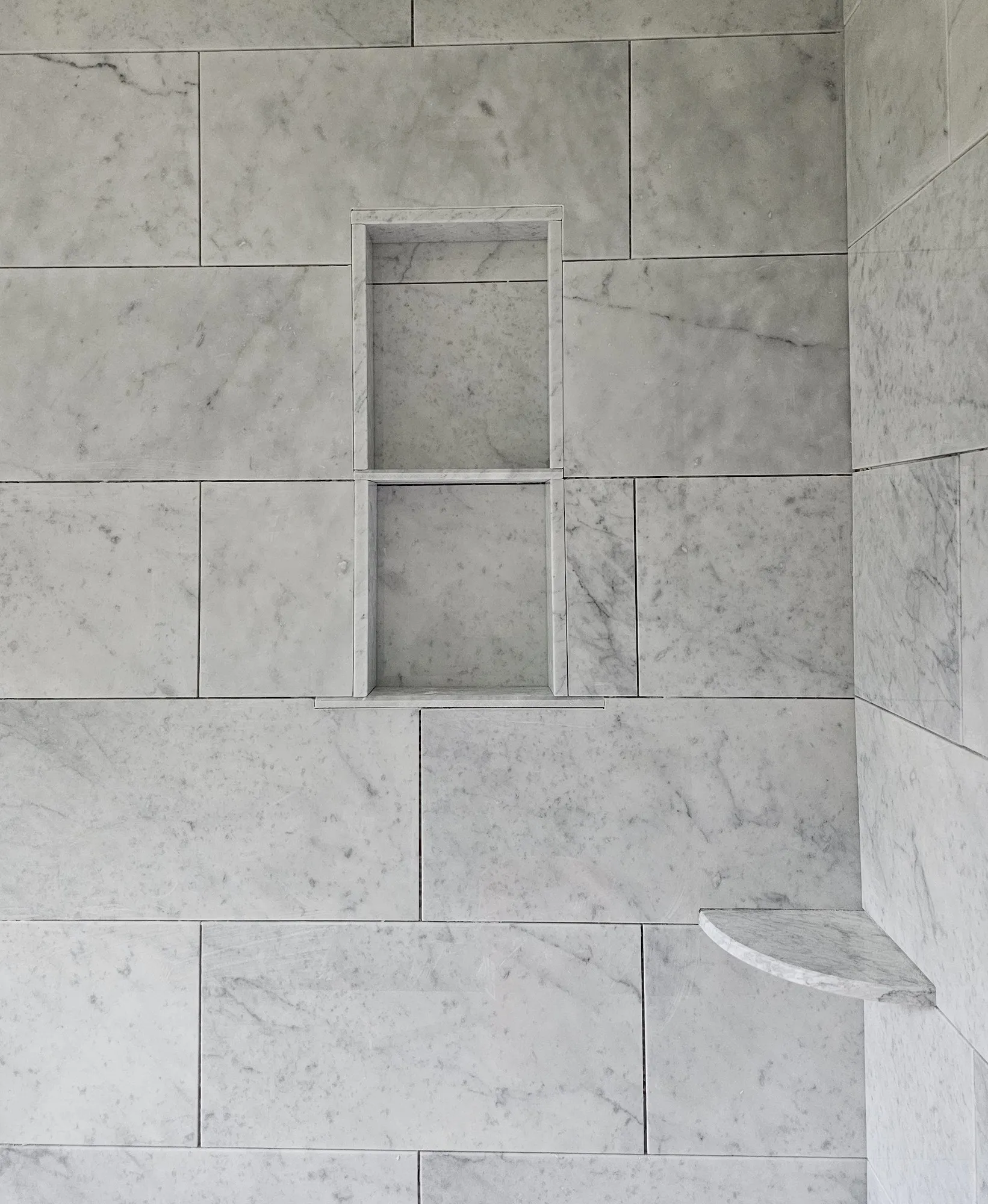 Carrara marble shower with a built-in niche and a corner shelf, installed by Euphoric Tile & Design in coastal Maine