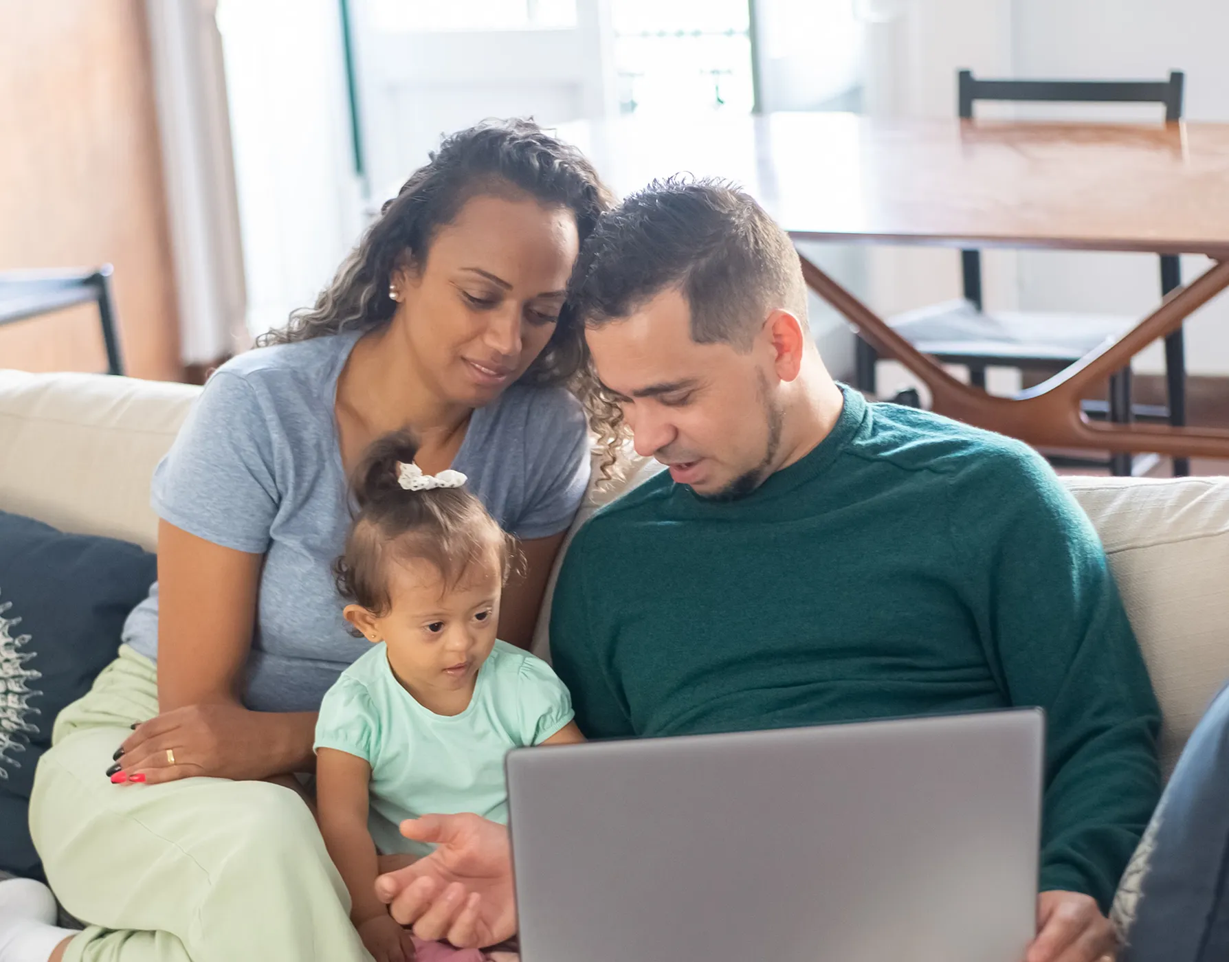 A family of three sitting on a couch looking at a laptop together in a living room.