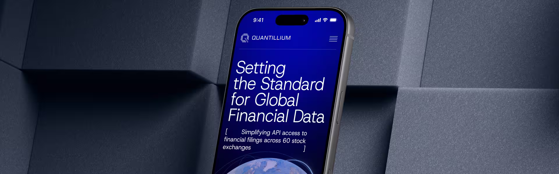Smartphone mockup tilted against a textured gray background, displaying the Quantillium website. The screen shows a deep blue hero section with the headline “Setting the Standard for Global Financial Data” and subtext about simplifying API access to financial filings across 60 stock exchanges, with the Quantillium logo at the top