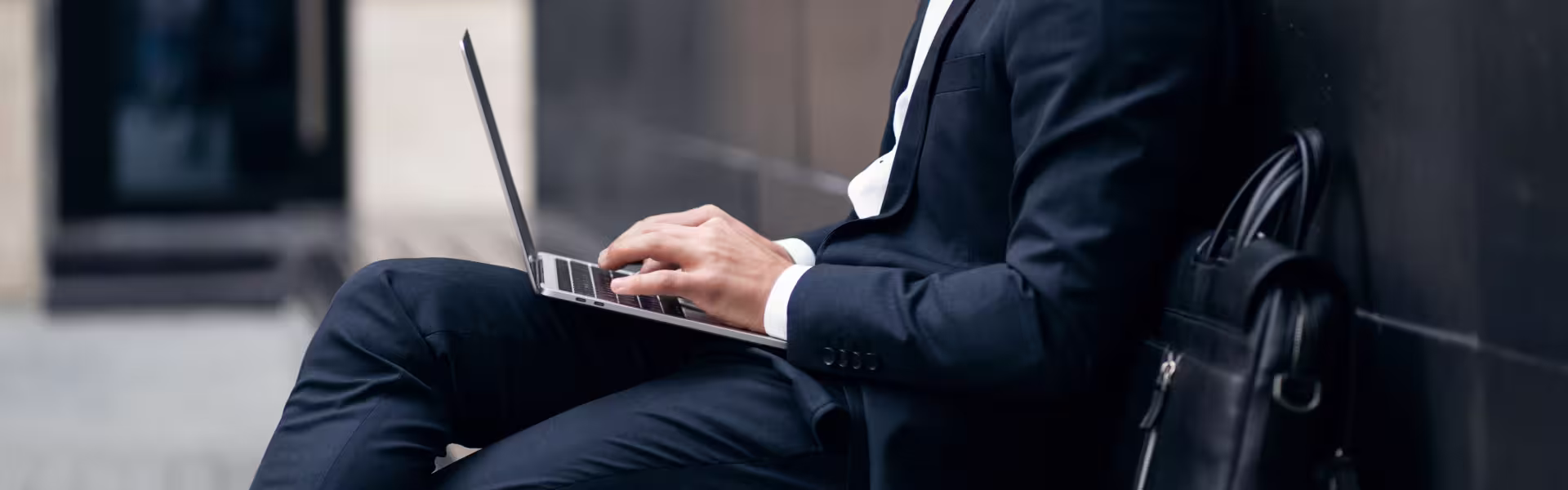 Business professional in suit using laptop outdoors, representing modern digital work and productivity