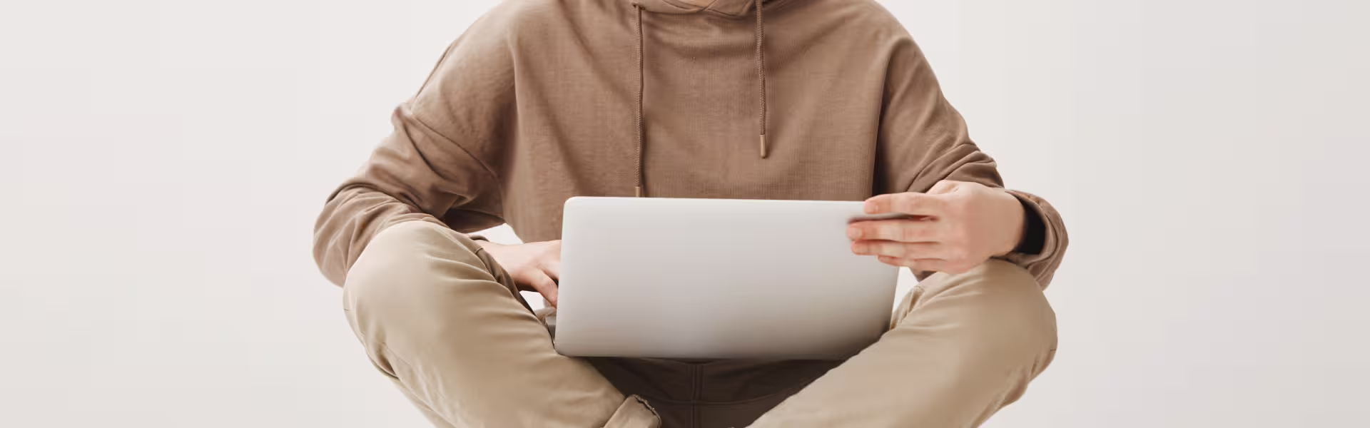 Young man in casual hoodie working on a laptop while sitting cross-legged, representing remote work and online learning