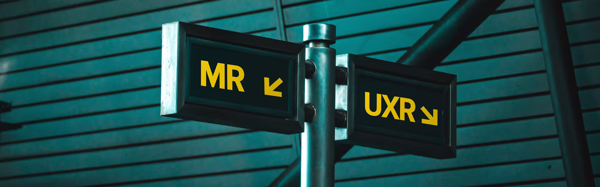 Directional signpost with two black signs and yellow letters: one pointing left labeled 'MR' and the other pointing right labeled 'UXR,' mounted on a metallic pole against a teal-toned background with horizontal paneling