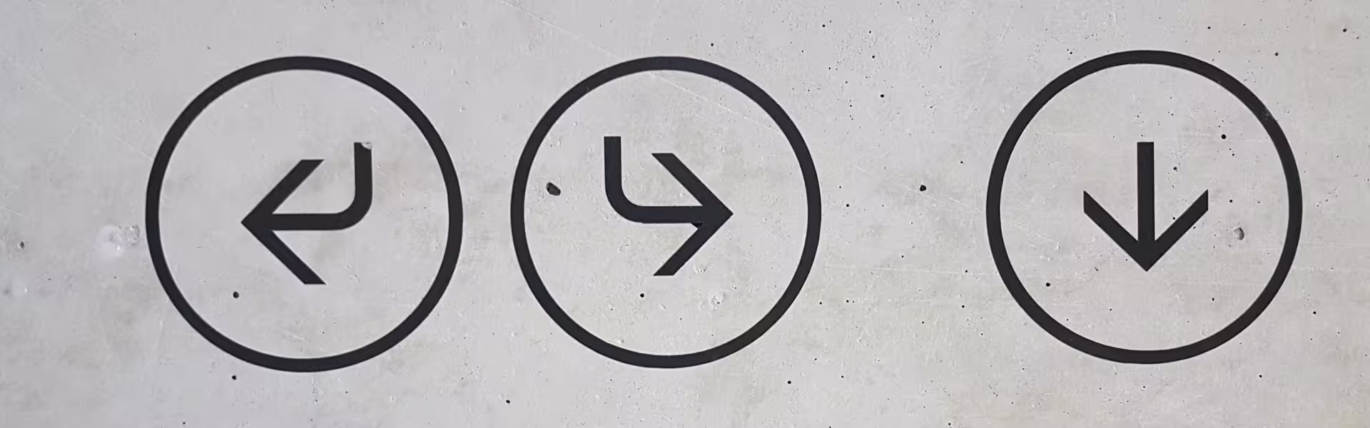 Minimalist black navigation arrow icons on concrete wall showing directions left, right, and down